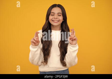 Zufrieden fröhlich Teenager Kind wünscht viel Glück, kreuzt die Finger, hat Vertrauen für besser, isoliert über gelben Hintergrund. Stockfoto