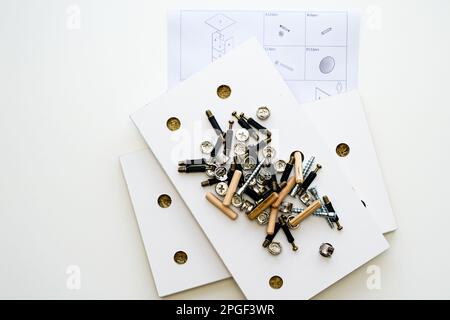 Möbelbeschläge. Ein Stapel verschiedener Montagezubehör auf einem weißen laminierten Spanplattenteil eines neuen Möbelstücks, Diagramm zur Selbstmontage von Möbeln Stockfoto