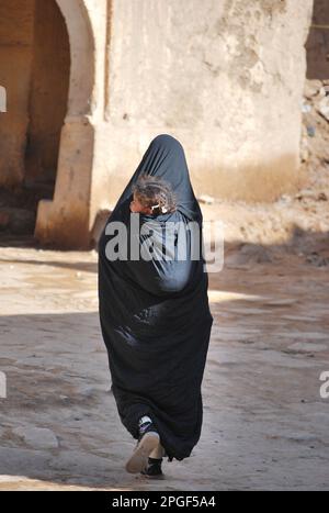 Eine Frau mit einem Chador, die mit ihrer Tochter auf den Schultern läuft, Marokko Stockfoto