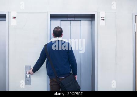 Rückansicht eines Geschäftsmanns, der in einem Büro den Aufzugknopf drückt, Freiburg im Breisgau, Baden-Württemberg, Deutschland Stockfoto