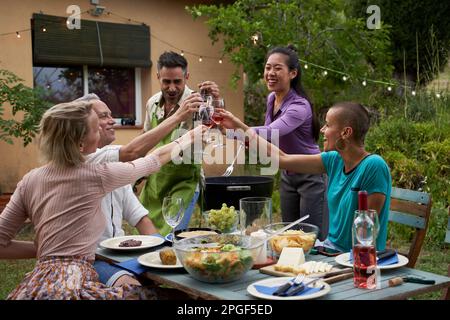 Fröhliche Freunde, die Spaß im Freien haben und zusammen im Garten wohnen. Freundschaftskonzept von Menschen mittleren Alters, die mit einem Glas Wein anstoßen. Stockfoto