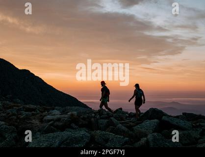 Zwei Wanderer wandern bei Sonnenaufgang auf dem Gipfel von Katahdin entlang. Stockfoto