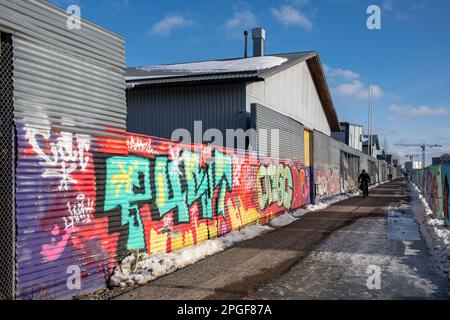 Industriehallen hinter einem mit Graffiti bedeckten Welleisenzaun im Bezirk Kyläsaari in Helsinki, Finnland Stockfoto