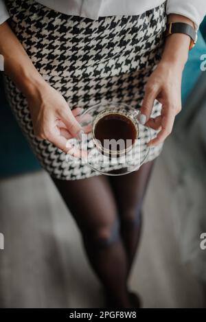 Frau in Arbeitskleidung hält eine Tasse frisch zubereiteten Kaffee. Stockfoto