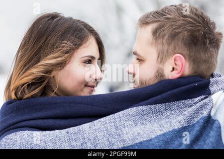 Ein Paar Liebhaber ist in einen blauen Schal eingewickelt, inmitten des Schneeparks Stockfoto