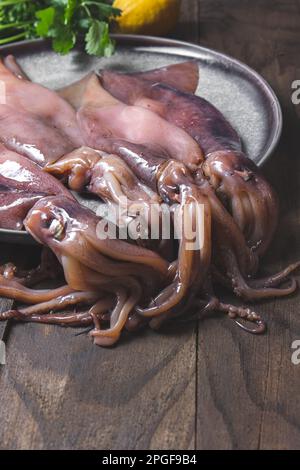 Rohe Kalmare auf grauen Platten mit Koriander und Zitronen. Auf dunklem Holzhintergrund. Stockfoto