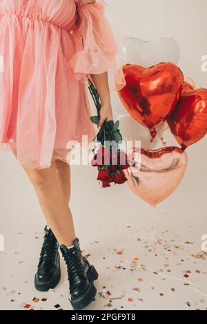 Nahaufnahme einer Frau mit roten Rosen bei Herzballons und Confetti Stockfoto