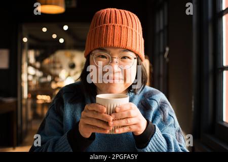 Porträt einer lächelnden asiatischen Frau mit einer heißen Tasse Kaffee Stockfoto