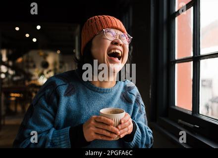 Eine Asiatin, die lacht und Kaffee in einem Café trinkt Stockfoto