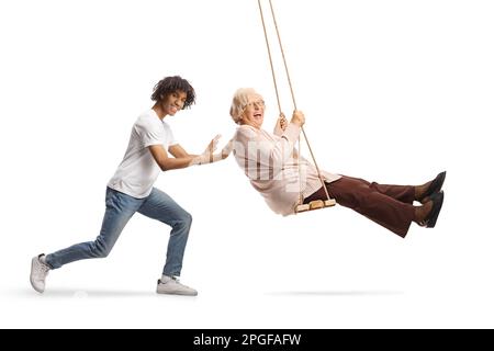 Junger afroamerikanischer Mann schubst eine weiße Seniorin auf eine Schaukel, isoliert auf weißem Hintergrund Stockfoto