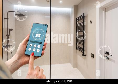 Nahaufnahme Smartphone in weiblicher Hand mit Smart-Home-System-App-Schnittstelle auf Handybildschirm, junge Frau, die alle Systeme des Hauses per Telefon steuert Stockfoto