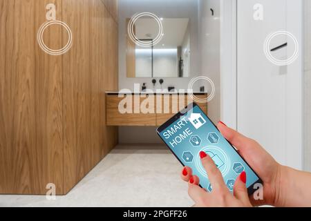Nahaufnahme Smartphone in weiblicher Hand mit Smart-Home-System-App-Schnittstelle auf Handybildschirm, junge Frau, die alle Systeme des Hauses per Telefon steuert Stockfoto