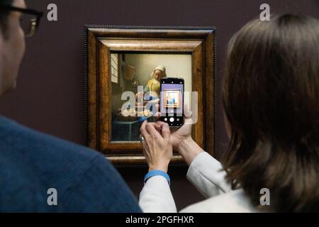 Amsterdam, Niederlande. 22. März 2023. Kunstliebhaber drängen sich um Vermeers Gemälde „die Milkmain“ im Rijksmuseum, und eine Frau macht ein Foto mit ihrem Handy. Die Show wird als ein einmaliges Erlebnis angesehen, in dem Vermeers Gemälde aus Museen auf der ganzen Welt zusammengeführt werden, und ist für die gesamte Show ausverkauft. Kredit: Anna Watson/Alamy Live News Stockfoto