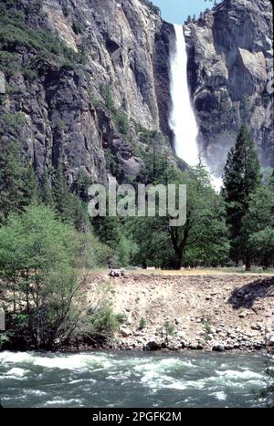 Yosemite-Nationalpark. CA. USA 1984. Yosemite Upper, Middle und Lower Falls. Halten Sie Ausschau nach dem Eiszapfen am Fuß des oberen Wasserfalls im Winter und nach dem brüllenden Abfluss von April bis Juni. Die Yosemite Falls, einer der höchsten der Welt, bestehen aus drei separaten Wasserfällen: Dem oberen Yosemite-Fall (1.430 Fuß), den mittleren Kaskaden (675 Fuß) und dem unteren Yosemite-Fall (320 Fuß). Die beste Aussicht auf die Yosemite Falls bietet die Gegend um Sentinel Meadow und die Yosemite Chapel. Nevada Falls, Bridalveil Falls und Vernal Falls vom Boden des Yosemite Valley aus gesehen. Stockfoto