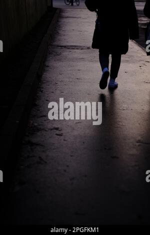 Ein vertikales Graustufenbild einer Person, die an einem Regentag die Straße entlang läuft Stockfoto