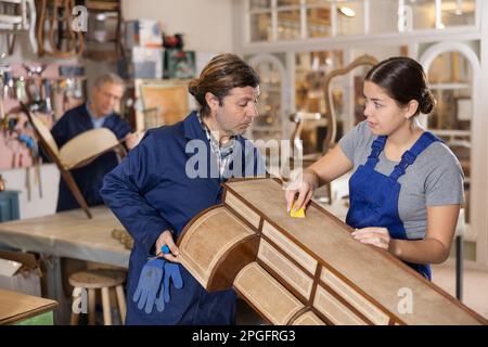 Professionelle Kunsthandwerker und Kunsthandwerker in Uniform renovieren antiken Kommoden während der Arbeit in der Reparaturwerkstatt Stockfoto