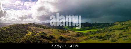 Panoramablick auf die helle Sonne und die dunklen Sturmwolken über der grünen kalifornischen Landschaft Stockfoto