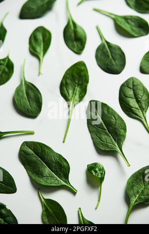 Frische Baby-Spinatblätter auf weißem Marmorhintergrund. Flach lat, Draufsicht. Kreatives Konzept, bei dem Spinatblätter mit einem rechteckigen Rahmen ausgekleidet sind. Stockfoto