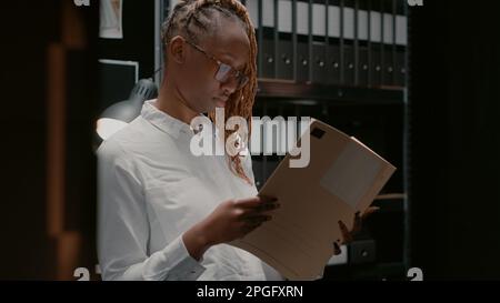 Privatdetektiv analysiert gesammelte Informationen in der Polizeibehörde. Eine Detektivin, die im Beweisraum sitzt und Archivakten liest, Hinweise und Fallakten studiert. Stockfoto