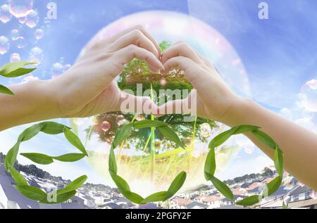 Ein konzeptionelles Bild, das die Ökologie darstellt, in dem Hände ein Herz bilden vor dem Hintergrund einer grünen Erde, umgeben von Gras. Stockfoto
