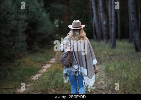 Frau mit Poncho, Cowboyhut und Rucksack, die im Wald spaziert Stockfoto