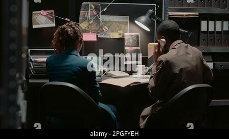 Privatdetektive untersuchen Überwachungsfotos und lesen Fallakten im Polizeibüro. Ein Detective, der verdächtige Beweise auf dem Laptop ansieht, ein Assistent, der Strafregister studiert. Stockfoto