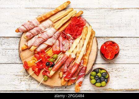 Brett mit leckerem italienischen Grissini mit Speck auf hellem Holzhintergrund Stockfoto