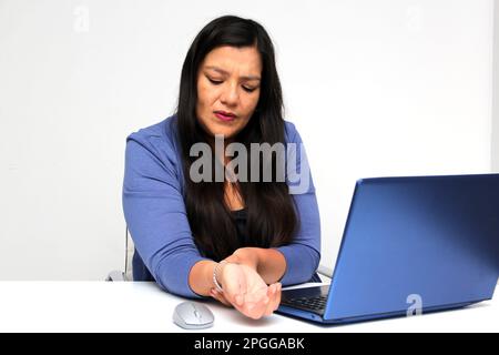 Erwachsene Latina-Frau, die unter Schmerzen, Kribbeln, Taubheitsgefühl und Schwäche im Handgelenk aufgrund eines Karpaltunnelsyndroms leidet, während sie in ihrer Praxis arbeitet Stockfoto