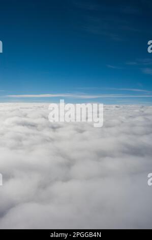 Aufgeblasene Wolken und blauer Himmel von oben in einem Flugzeug Stockfoto