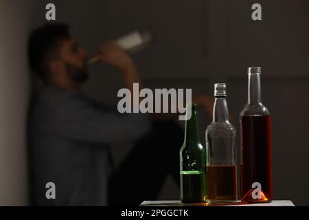 Ein abhängiger Mann, der drinnen an der Wand sitzt, konzentriert sich auf einen Tisch mit alkoholischen Getränken. Platz für Text Stockfoto