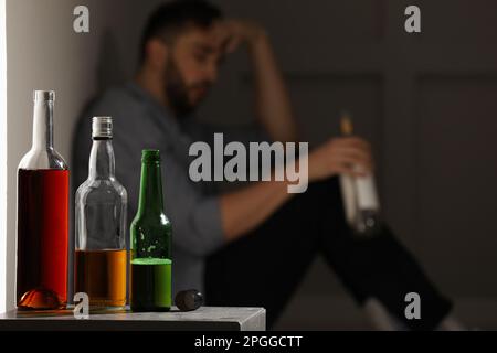 Ein abhängiger Mann, der drinnen an der Wand sitzt, konzentriert sich auf einen Tisch mit alkoholischen Getränken. Platz für Text Stockfoto