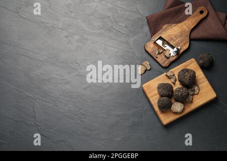 Holzrasierer mit ganzen und geschnittenen Trüffeln auf schwarzem Tisch, flach liegend. Platz für Text Stockfoto