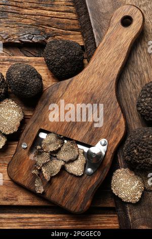 Rasierer mit ganzen und geschnittenen schwarzen Trüffeln auf einem Holztisch, flach liegend Stockfoto