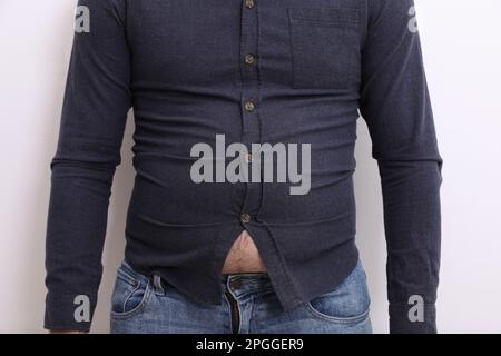 Ein Mann mit einem engen Hemd auf weißem Hintergrund, Nahaufnahme. Übergewichtigkeitsproblem Stockfoto