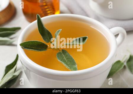 Tasse aromatischer Salbeitee mit frischen Blättern auf dem Tisch, Nahaufnahme Stockfoto