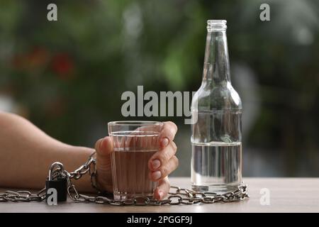 Ein Mann an ein Glas Wodka am Tisch gekettet vor verschwommenem Hintergrund, Nahaufnahme. Alkoholsucht Stockfoto