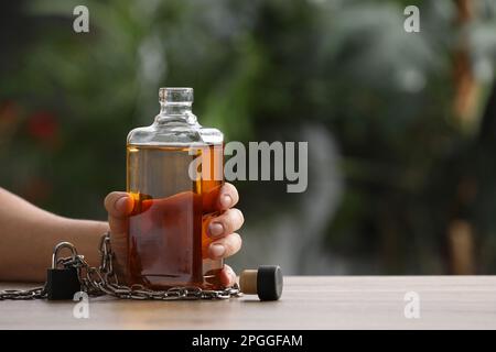 Abhängiger Mann gekettet an eine Flasche alkoholischen Getränks am Tisch vor verschwommenem Hintergrund, Nahaufnahme. Platz für Text Stockfoto