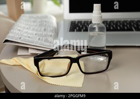 Brille, Mikrofasertuch und Sprühflasche auf dem Tisch im Innenbereich Stockfoto