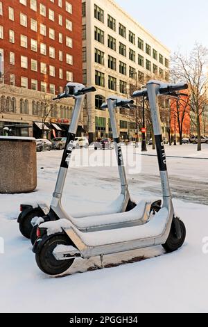 Drei ELEKTRISCHE VOGEL-Roller, die nach einem schweren Schneefall an einer Straßenecke in der Innenstadt von Cleveland, Ohio, mit Schnee bedeckt sind. Stockfoto