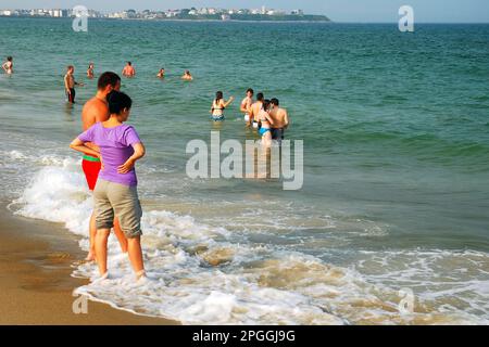 Ein junges Paar waten entlang der Küste, während die Meereswellen an einem Sommerurlaubtag in Hampton Beach, New Hampshire, auf ihren Füßen krachen Stockfoto