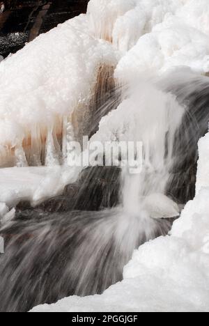 An einem kalten Wintertag fällt ein Wasserfall trotz der oberen Schicht aus gefrorenem Eis weiter Stockfoto