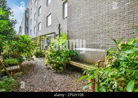 Ein Außenbereich mit Pflanzen und Holzbänken im mittleren Teil des Gartens, neben einer Ziegelwand Stockfoto