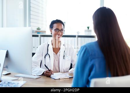 Du siehst so gut aus seit unserer letzten Untersuchung. Eine junge Ärztin, die mit einer Patientin in ihrem Sprechzimmer spricht. Stockfoto