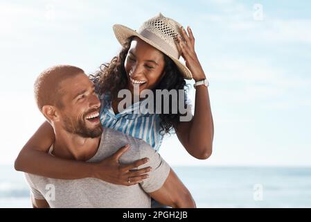 Es gibt nur Glück in meinem Leben, wenn ich bei dir bin. Ein junger Mann, der seine Freundin am Strand mit dem Huckepack versorgte. Stockfoto