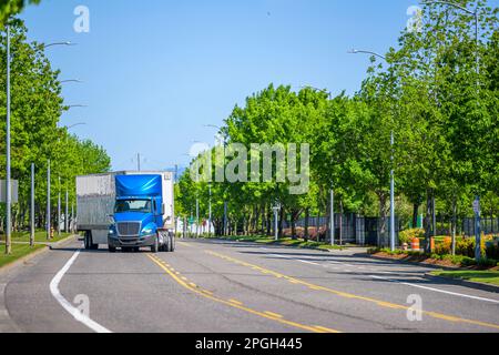 Big Rig Classic leistungsstarker langer Lkw-Sattelzugmaschine in Blau mit Dachspoiler transportiert kommerzielle Fracht in einem trockenen Auflieger, der die CI einschaltet Stockfoto