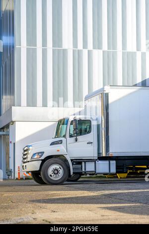 Industrieller Sattelzugmaschine mit Nahverkehrsfahrerhaus und Anhänger mit Kastenwagen für Trockenwagen steht auf dem Parkplatz des Lagerlagers und wartet auf den Start des nächsten Frachtes Stockfoto