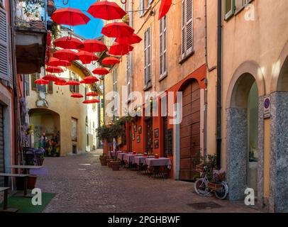 Luino, Italien - 16. März 2023: Kopfsteingepflasterte Straße mit kleinen Geschäften und farbenfrohen Dekorationen im alten Stadtzentrum von Luino Stockfoto