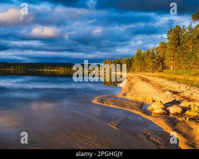 Eine abendliche Landschaft des Femunden-Sees in Norwegen, die einen ruhigen Sommerhimmel widerspiegelt und von Sand, Bäumen und Wildnis umgeben ist. Stockfoto