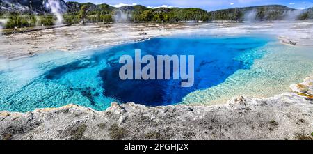 Ein malerischer Blick auf einen großen Thermalpool mit leuchtend blauem Wasser, das aus den Tiefen sprudelt und Dampf von der Oberfläche aufsteigt Stockfoto