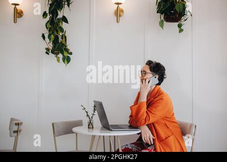 Erfolgreiche Geschäftsfrau, die telefoniert, während sie an einem entfernten Standort arbeitet. Reife Geschäftsfrau, die während eines Telefongesprächs mit einem glücklich lächelt Stockfoto